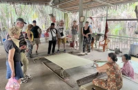 Khách du lịch nước ngoài theo dõi công đoạn dệt chiếu tại xã Nhơn Thạnh (thành phố Bến Tre, tỉnh Bến Tre).