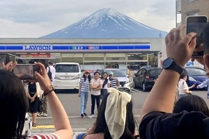 Khách du lịch chụp ảnh với khung cảnh núi Phú Sĩ phía sau cửa hàng tiện lợi Lawson ở thị trấn Fujikawaguchiko, tỉnh Yamanashi, Nhật Bản, ngày 28/4/2024. (Ảnh: Reuters/Kyodo) 