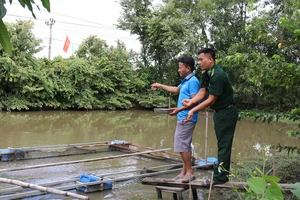 Đại úy Lê Văn Hải, cán bộ Đồn Biên phòng Yok M’Bre hướng dẫn hộ dân kỹ thuật chăm sóc cá thát lát đúng cách. (Ảnh: BÍCH NGUYÊN)