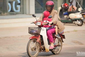 Người dân Lào tìm cách hạn chế nắng nóng khi tham gia giao thông. Ảnh: Hải Tiến