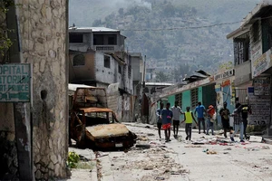Người dân đi ngang qua chiếc ô-tô bị hư hỏng ở khu Carrefour Feuilles, nơi bị bỏ hoang do bạo lực băng đảng tại thủ đô Port-au-Prince, Haiti, ngày 19/3/2024. (Ảnh: Reuters)