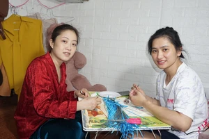 Chị Trang (bên phải) và chị Xiêm nỗ lực làm tranh cuốn giấy, vừa để kiếm thêm tiền trang trải chi phí, vừa để quên đi phần nào bệnh tật.