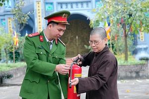 Cán bộ Công an xã Yên Mỹ, huyện Thanh Trì, Hà Nội hướng dẫn ni sư chùa Thanh Lan sử dụng bình cứu hỏa. Ảnh: HUY HOÀNG