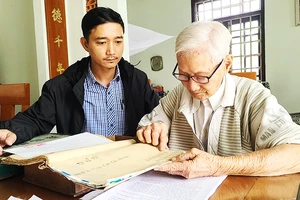 Cụ Hà Thúc Duyên lần dở cuốn địa bạ thời Vua Gia Long. 