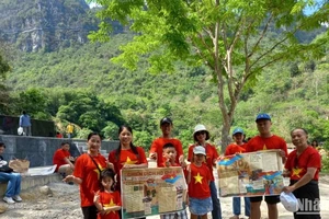 Du khách mang theo phụ san của Báo Nhân Dân về Chiến dịch Hồ Chí Minh, check-in tại thác Bản Giốc, xã Đàm Thủy, huyện Trùng Khánh, tỉnh Cao Bằng.