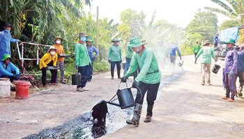 Các thành viên của Đội vá đường thiện nguyện huyện Chợ Mới đổ nhựa đường, thi công đoạn đường nông thôn xuống cấp.