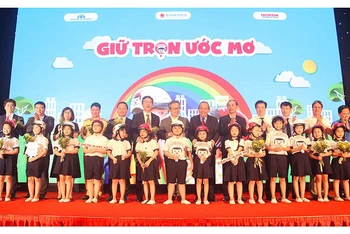 Phó Thủ tướng Trương Hòa Bình và các đại biểu trao tượng trưng mũ bảo hiểm đạt chuẩn cho các học sinh lớp một tại lễ công bố chương trình “Giữ trọn ước mơ” ngày 3-7.