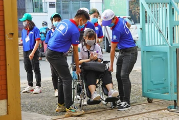 Các tình nguyện viên hỗ trợ một thí sinh phải ngồi xe lăn.