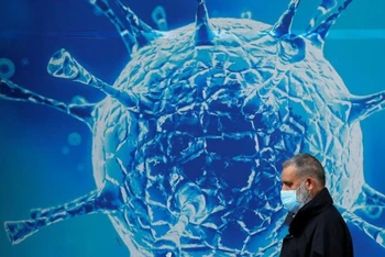 Một người đàn ông đeo khẩu trang đi ngang qua hình ảnh minh họa của virus SARS-CoV-2 bên ngoài một trung tâm khoa học ở Oldham, Anh ngày 3-8-2020. Ảnh: Reuters.