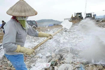 Công nhân Công ty TNHH MTV Môi trường đô thị Hà Nội rắc chế phẩm khử mùi tại bãi rác Nam Sơn. (Ảnh: KHÁNH SƠN)