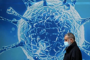 Một người đàn ông đeo khẩu trang đi qua hình minh họa virus SARS-CoV-2 bên ngoài một trung tâm nghiên cứu khoa học ở Anh. Ảnh: Reuters.