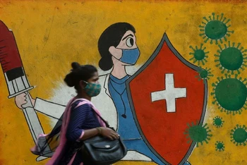 Người phụ nữ đi qua bức tường có tranh cổ động người dân tiêm phòng Covid-19 tại Mumbai, Ấn Độ. (Ảnh: Reuters)