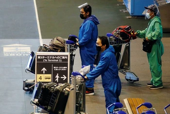 Hành khách mặc đồ bảo hộ di chuyển tới điểm chờ xe buýt tại sân bay quốc tế Narita, Nhật Bản, ngày 30/11. (Ảnh: Reuters)