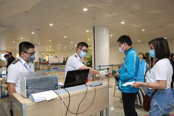 Nhân viên y tế kiểm tra phiếu khai báo y tế của hành khách trước khi làm thủ tục nhập cảnh tại cửa khẩu Sân bay quốc tế Nội Bài (Ảnh: TTXVN)