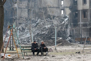 Người dân địa phương ngồi gần một tòa chung cư tại TP Mariupol, Ukraine, ngày 25/3. (Ảnh: Reuters)