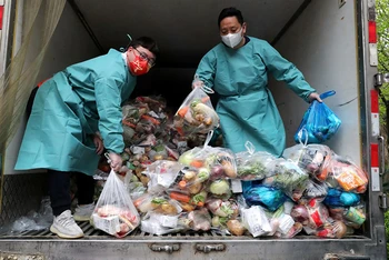 Nhân viên mặc đồ bảo hộ xếp thực phẩm lên xe tải để phân phát cho người dân. (Ảnh: China Daily)