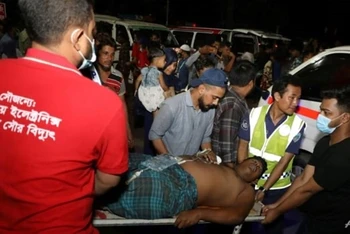 Các nhân viên cứu hộ và dân thường khiêng một nạn nhân bị thương tới bệnh viện ở Chittagong, Bangladesh, sau khi đám cháy lớn bùng phát tại một kho cảng container địa phương. (Nguồn: AFP/Vietnam+)