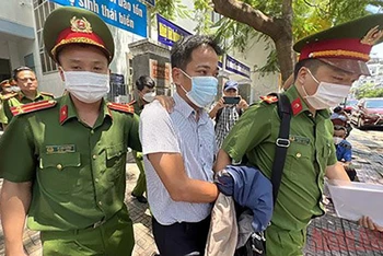 Cảnh sát áp giải ông Trần Quốc Huy, Trưởng Phòng Tổ chức-Hành chính CDC Khánh Hòa rời khỏi trụ sở làm việc. (Ảnh: THÀNH LONG)
