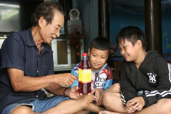Nghệ nhân Trần Ngọc Vinh và các cháu bên sản phẩm nước mắm của gia đình. 