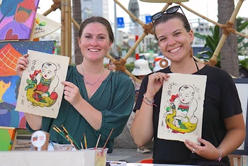 Các chị Kassidee và Izzy (du khách Mỹ) thích thú khi trải nghiệm làm tranh Ðông Hồ tại Lễ hội Tận hưởng mùa hè 2023-Enjoy Danang 2023. 