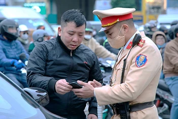 Cán bộ Cảnh sát giao thông, Công an thành phố Hà Nội trao đổi, hướng dẫn người dân tuân thủ pháp luật khi tham gia giao thông. (Ảnh: NAM PHONG)