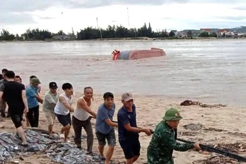 Bộ đội biên phòng và người dân hợp sức neo buộc tàu cá bị lật chờ nước lũ sông Gianh giảm để trục vớt.