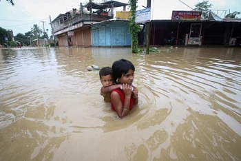 Một bé gái cõng em trai lội qua con đường ngập nước sau trận mưa lớn ở ngoại ô thành phố Agartala, Ấn Độ, ngày 18/6/2022. (Ảnh minh họa: Reuters)