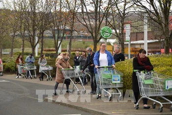 Người dân thực hiện giãn cách xã hội phòng lây nhiễm Covid-19 khi xếp hàng chờ mua sắm bên ngoài 1 siêu thị ở Gateshead, Anh, ngày 9/4/2020. (Ảnh: AFP/TTXVN)