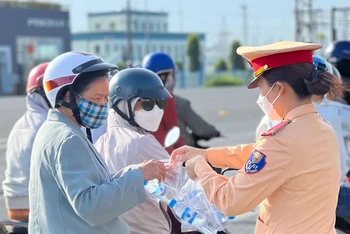 Nữ chiến sĩ Cảnh sát giao thông Công an tỉnh Đồng Nai phát nước suối, khăn lạnh cho người dân.