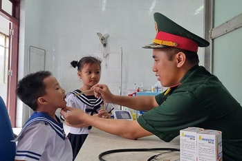 Đại úy, Bác sĩ, Thạc sĩ Lê Văn Quốc, Bệnh xá trưởng đảo Song Tử Tây thăm khám cho cháu Phan Gia Phát (4 tuổi).