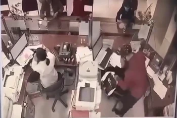 Tên cướp mặc áo sẫm đỏ (bên phải ảnh) đang khống chế nhân viên ngân hàng. (Ảnh cắt từ video)