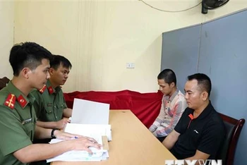 Lực lượng chức năng lấy lời khai bị can Nguyễn Quang D. (áo đen) và bị can Đinh Tiến S. (áo kẻ). (Ảnh: Phạm Kiên/TTXVN)
