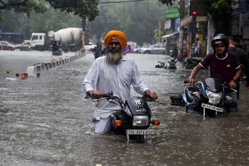 Người dân cùng phương tiện giao thông vượt qua tuyến đường bị ngập tại New Delhi, ngày 8/7/2023. (Ảnh: Reuters)