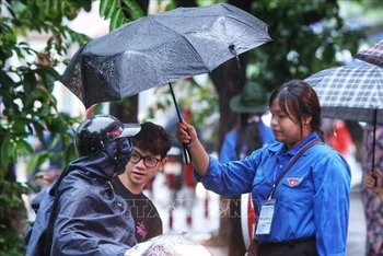 Tình nguyện viên hỗ trợ đón thí sinh vào điểm thi trong cơn mưa sáng 9/1 (Ảnh: TUẤN ANH/TTXVN)