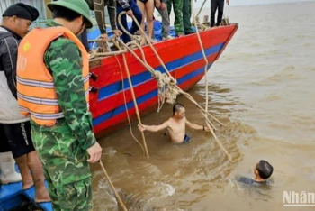 Huy động thợ lặn xuống nước buộc dây để lai dắt tàu cá bị chìm vào bờ.