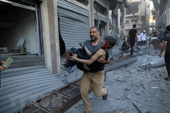 Người đàn ông bế một em nhỏ bị thương sau cuộc không kích của Israel xuống Dải Gaza. (Ảnh: THX/TTXVN)