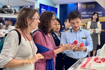 Cán bộ Tổng cục Quản lý thị trường hướng dẫn khách du lịch người nước ngoài phân biệt các sản phẩm thật-giả.