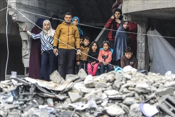 Người dân Palestine đứng trên đống đổ nát của những tòa nhà bị phá hủy sau các cuộc không kích của Israel xuống Dải Gaza. Ảnh: THX/TTXVN