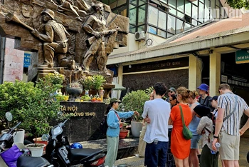 Du khách nước ngoài tìm hiểu về ý nghĩa của bức phù điêu “Hà Nội mùa đông năm 1946” trước cổng chợ Đồng Xuân, Hà Nội. (Ảnh: T.LINH)