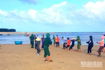Bộ đội Biên phòng và người dân hỗ trợ anh Phạm Thanh Huân kéo thuyền đánh cá bị nạn vào bờ.