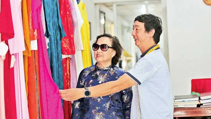 Thợ may Nguyễn Quốc Hòa (bên phải) giúp khách hàng thử áo dài.