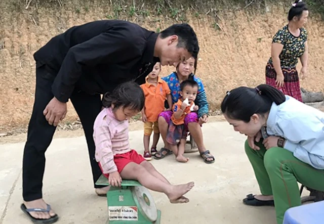 Cán bộ Trung tâm y tế huyện Tủa Chùa kiểm tra cân nặng của trẻ em trong vùng. 