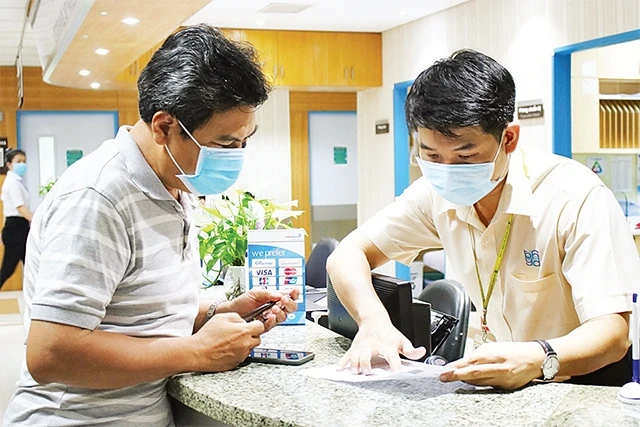 Nhân viên Bệnh viện Đại học Y Dược TP Hồ Chí Minh hướng dẫn người nhà bệnh nhân thanh toán viện phí không dùng tiền mặt.