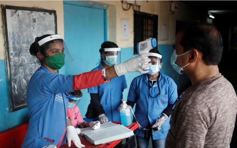 Nhân viên y tế đo thân nhiệt cho người dân tại một trường học ở Mumbai, Ấn Độ, ngày 10-8. (Ảnh: Reuters)