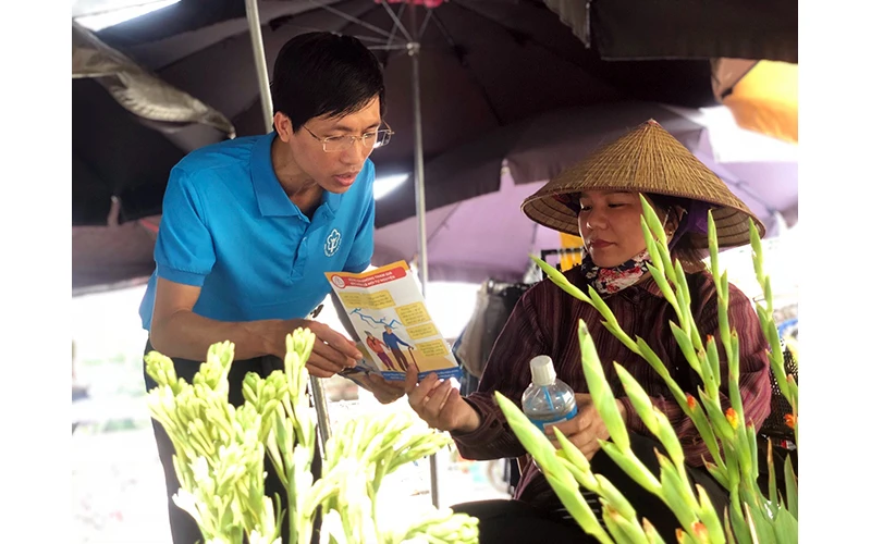 Cán bộ BHXH Ninh Bình tuyên truyền chính sách BHYT; BHXH tự nguyện cho tiểu thương trong chợ. Ảnh: NINH BÌNH 