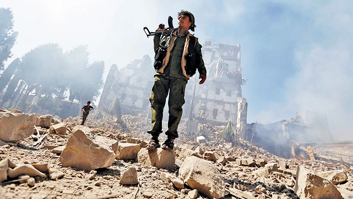 Một tay súng Houthi trước tòa nhà đổ nát sau trận không kích của liên quân Hồi giáo. Ảnh: ARAB NEWS