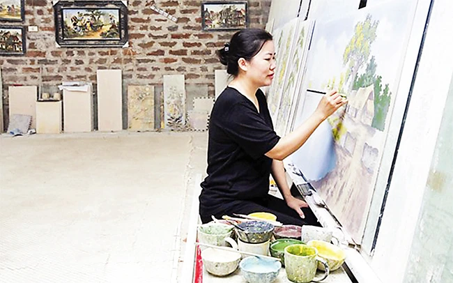 Chị Lê Thị Chuyên (xã Kim Lan, huyện Gia Lâm) hoàn thiện sản phẩm tranh gốm sứ ghép miếng tại cơ sở sản xuất gia đình. Ảnh: NGỌC MINH
