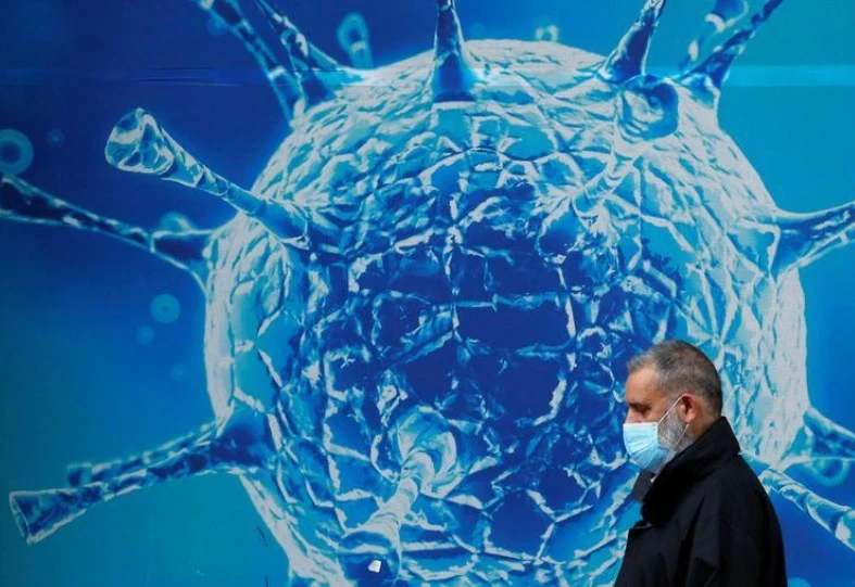 Một người đàn ông đeo khẩu trang đi ngang qua hình ảnh minh họa của virus SARS-CoV-2 bên ngoài một trung tâm khoa học ở Oldham, Anh ngày 3-8-2020. Ảnh: Reuters.