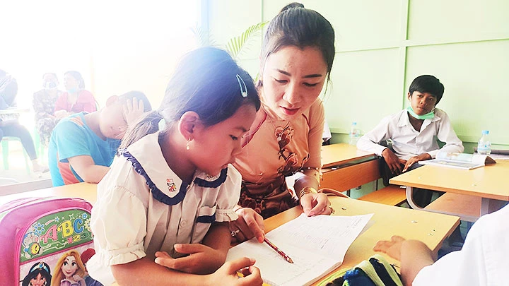 Cô giáo Dương Kim Huệ giúp bé làm quen với chữ Việt.