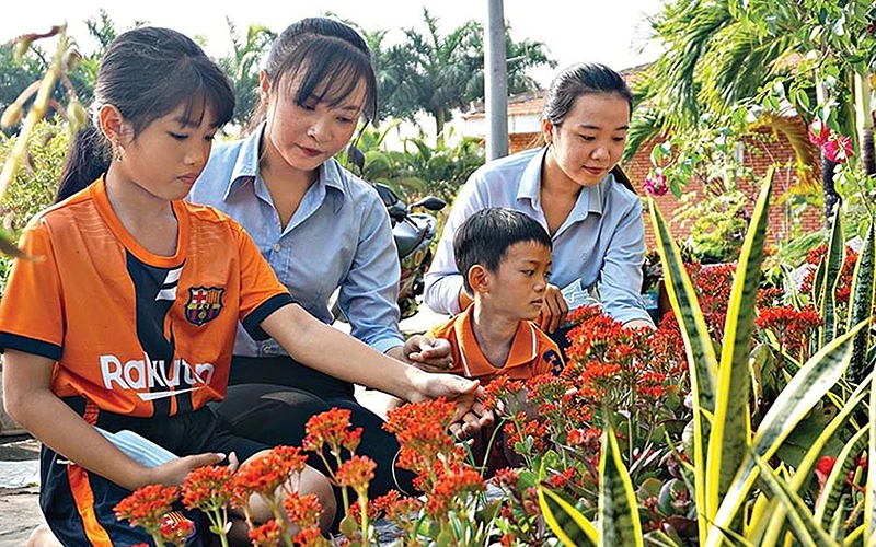 Sinh viên Trường cao đẳng Cộng đồng Cà Mau hướng dẫn các em nhỏ Làng trẻ em SOS (phường 5, TP Cà Mau, tỉnh Cà Mau) chăm sóc hoa trong vườn. Ảnh: YẾN NHI
